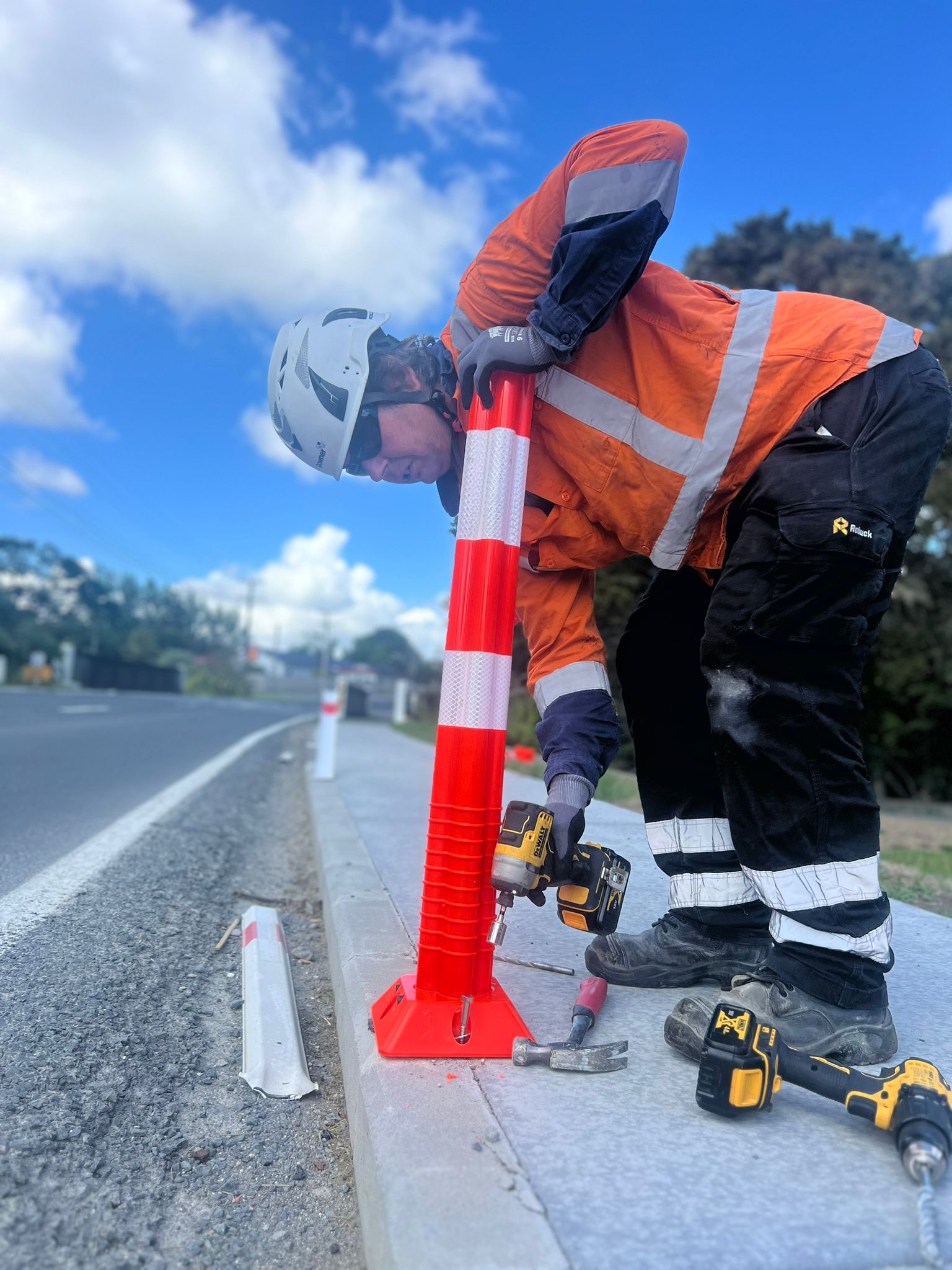 A road worker installing bright orange 'hit sticks' on the side of the road in Paparoa